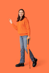 Poster - Happy young woman with umbrella on orange background