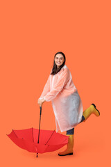 Poster - Happy young woman in raincoat and with umbrella on orange background