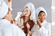 © Prostock-studio - Multiracial happy girlfriends in bathrobes getting ready for party, putting make up in front of big mirror at home