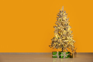 Canvas Print - Decorated Christmas tree with glowing lights and gift boxes near yellow wall