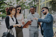 © qunica.com - A multicultural group of business people having an outdoor meeting in the city. They are discussing projects, brainstorming ideas, and strategizing for sales growth while analyzing documents.