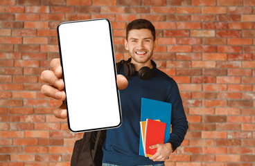 Poster - Modern Student. Happy Guy With Backpack Holding Smartphone And Notebooks Smiling To Camera Standing Over Brick Wall Background Indoor