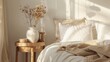 © Sam - A close-up of a bedside table with a vase of dried flowers, a wooden candle holder, and a small wooden box. The bed is made with white bedding and a tan throw.