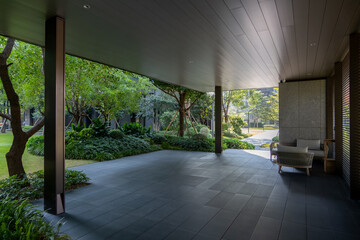 A modern outdoor patio with stone slabs features a covered area with wooden beams. Comfortable seating area with armchairs in the corner, an inviting public space for relaxation with a garden view