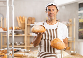 Adult male baker in uniform holding fresh homemade bread