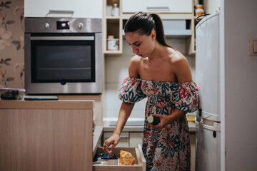 A young woman in a floral dress is preparing a meal in a modern kitchen. She looks focused and relaxed, suggesting a warm and welcoming atmosphere. Ideal for cooking or lifestyle themes.