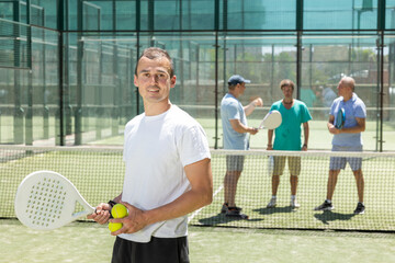 Wall Mural - Young athletic man padel tennis player posing with ball and racket on tennis court