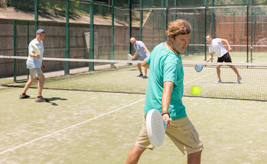 Two adult men doubles playing against two men in padel tennis on court