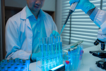 a scientist and his assistant are working together in the laboratory with a lot of science equipments such as microscope, test tube, beaker, pipette, two scientists work in the workplace