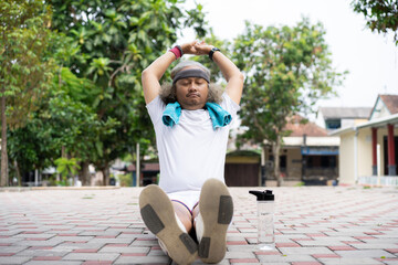 curly-haired adult Indonesian male who seems to struggle when warming up before exercise, the concept of a healthy lifestyle, warming up and cooling down before or after exercise.