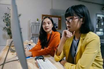 Two young professional women work late in a modern office, collaborating on a project. They focus on brainstorming ideas and finding solutions, embodying teamwork and support