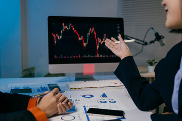 Two businesswomen are having a discussion about stock market investments, using graphs displayed on a computer screen to analyze trends and make informed decisions