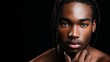 © Mickael - Close-up portrait of a young man with braided hair, hand resting on chin, looking directly at camera, against a dark background, focusing on facial details and expression.