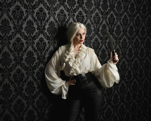 close up portrait of beautiful blonde female model, wearing vintage gothic fantasy ruffle blouse white shirt, leather pants, blonde hair holding knife weapon. moody black brocade wallpaper background