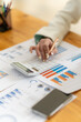 © Nittaya - Financial Analysis: Close-up of a woman's hand using a calculator and analyzing financial charts and graphs.