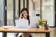 © Nittaya - Businesswoman Analyzing Data: A professional woman is meticulously analyzing data on a document while seated at her desk, laptop and other office supplies beside her.