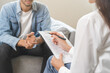 © KMPZZZ - Psychology, depression. Happy smile asian young man patient mental therapy explain symptom with psychologist while doctor woman taking notes at clinic. Psychologist with sick mental health person.