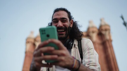 Hispanic man in joy using mobile phone for online communication while chatting online with friends. Happy tourist man enjoying roaming 5g network while reading funny message on his cellphone
