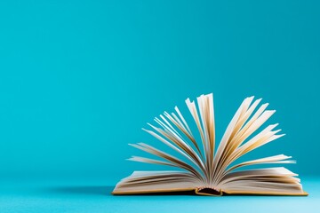 Book is laid open on a blue surface, with the pages spread wide open. blue background contrasts with the white pages of book, creating a sense of calm. The open book invites the viewer to explore