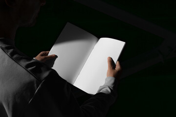 Man holding a blank open brochure mockup template in an urban outdoor environment with sharp sunlit shadows. Isolated surface to place your design. 