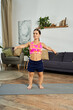 © LIGHTFIELD STUDIOS - A young brunette woman with a short stature exercises at home, lifting weights and enjoying a fitness routine in a stylish living room.