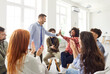 © Studio Romantic - Diverse group of happy young people in casual wear sitting on chairs in circle and applauding with man and woman giving high five to each other. Team celebrating successful collaboration and teamwork