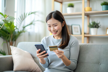 Wall Mural - Happy asian woman buying electronic services  application using card and smartphone sitting sofa at home.png