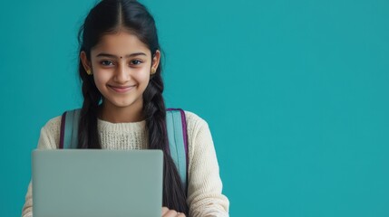 Happy Indian teen girl using a laptop for online studies on a blue background with ample copy space