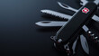 © Nata - A black background with a silver and black multi-tool. The tool is a Swiss Army knife with a serrated edge