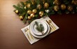 © joeycheung - A single place setting with gold flatware and a sprig of pine on a white plate sits on a brown wooden table with a garland of green pine branches and gold ornaments above.