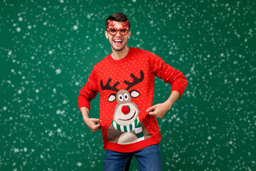 Wall Mural - Portrait of attractive cheerful guy having fun showing deer jumper winter festive isolated over green color background