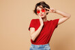 © ViDi Studio - Young smiling happy fun woman she wear red t-shirt casual clothes sunglasses cover eye with victory sign look camera isolated on plain pastel light beige background studio portrait. Lifestyle concept.