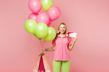 Poster - Young woman wear shirt celebrate birthday holiday, hold bunch of air balloons, shopping package bags store gift coupon voucher card isolated on plain pink background Black Friday sale buy day concept