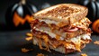 © familymedia - Grilled sandwich loaded with bacon, cheese and eggs, set against a festive Halloween backdrop featuring carved pumpkins, evoking warmth and seasonal celebration.