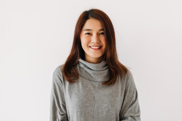 Happy beautiful asian Thai woman wear grey sweater, smiling while standing isolated over white wall in winter.