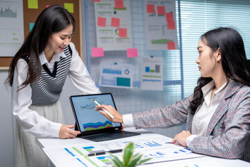 Two businesswomen working with charts and graphs on tablet and papers in modern office