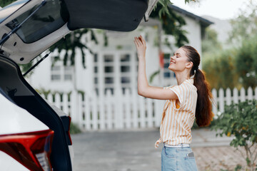 woman loading a car trunk, cheerful expression, casual attire, outdoor setting, home background, greenery ambiance, sunny day, organized travel preparations, lifestyle image, transportation concept