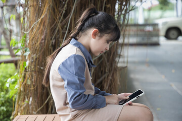 Smartphone and bad body posture concept, young Asian primary schoolgirl using smartphone with humpback or hunchback, incorrect body posture that might lead to curved, deformed spinal bone