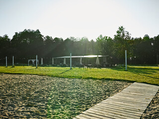 The photograph captures a sunny outdoor scene with a grassy field, sandy area, and a wooden walkway.