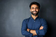 © SejutaCahaya - A young man with a beard and a blue shirt smiles confidently with his arms crossed, standing in front of a dark grey background.