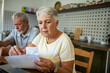© Marko Geber - Concerned senior couple reading bills on kitchen table with laptop