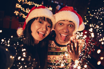 Portrait of two young people couple make selfie show tongue celebrate xmas new year garland lights flat indoors