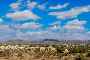 Scenic view of Oman\'s mountainous landscape with traditional architecture and palm trees under a bright sky