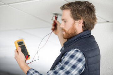 Wall Mural - man electrician in uniform measures voltage