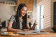 © kenchiro168 - young woman enjoys quiet moment in modern kitchen, reading book while holding cup. warm sunlight creates cozy atmosphere, enhancing her joyful expression