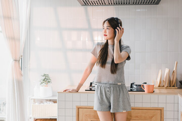 Enjoying music in modern kitchen, young woman in casual gray attire listens to her headphones. bright space features stylish design, creating relaxed vibe