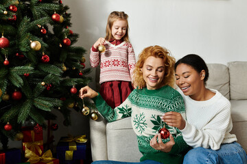 The family laughs together while adding ornaments to their Christmas tree at home.