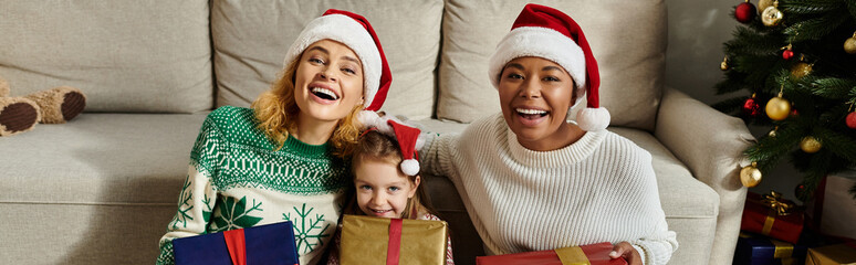 Wall Mural - Two mothers and their daughter share laughter and gifts while celebrating the holidays together.