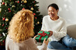 © Bliss - Two women exchange a beautifully wrapped gift amidst cozy holiday decorations and joy.