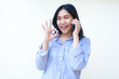 © M Alfan Setyawan - excited asian woman wearing striped shirt show okay signs while having a call on mobile phone isolated on white background